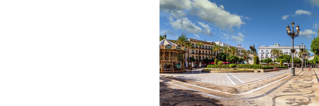 A square surrounded by palm trees and several buildings. In the foreground on the left is a vintage merry-go-round, while a statue, well-kept green spaces and decorative streetlights adorn the square.