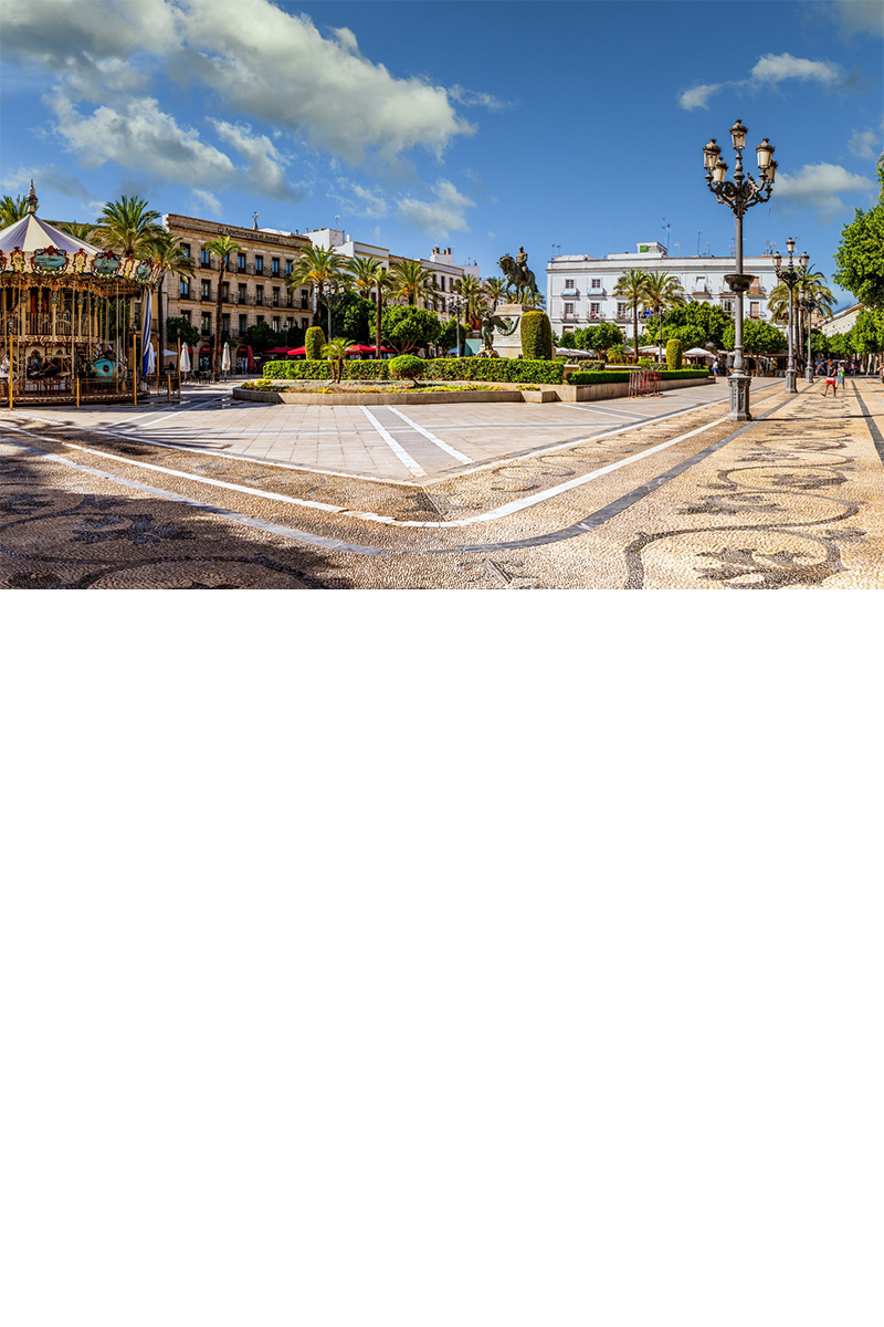 A square surrounded by palm trees and several buildings. In the foreground on the left is a vintage merry-go-round, while a statue, well-kept green spaces and decorative streetlights adorn the square.