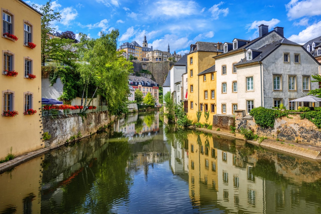 The Alzette River surrounded by buildings, trees and walls, with a view of the Upper Town 