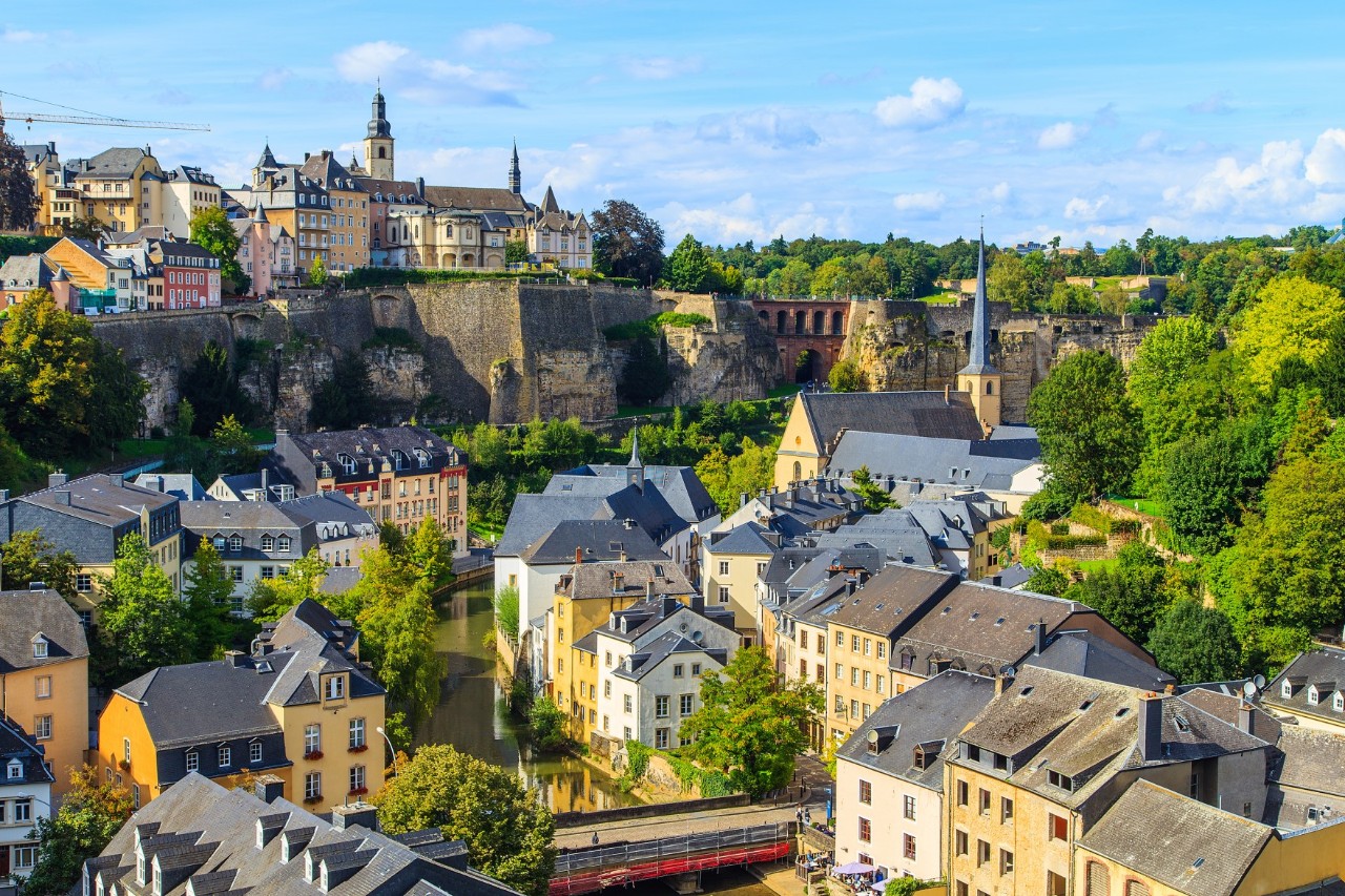 Panoramic view of Luxembourg City, elevated fortress wall, old buildings, church towers and green trees 