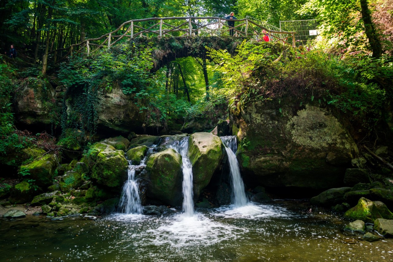 Waterfall in three streams with bridge, rocks and forest 