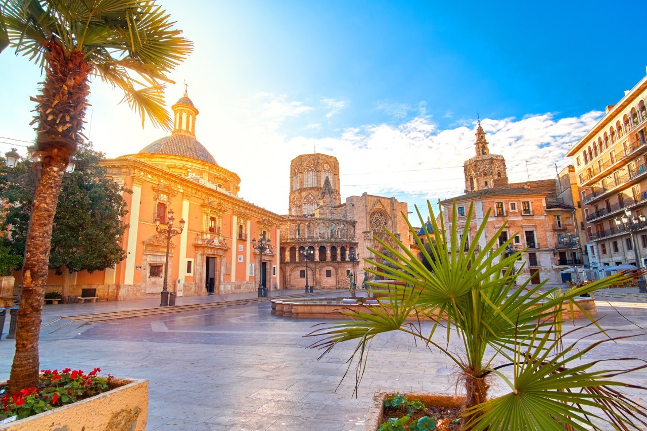 Deserted square with magnificent buildings, church towers and palm trees in the sunshine 