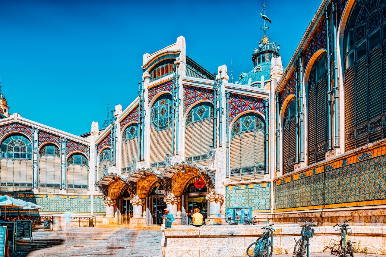 Exterior view of the market hall with a multi-coloured façade and  some seated people and bicycles 
