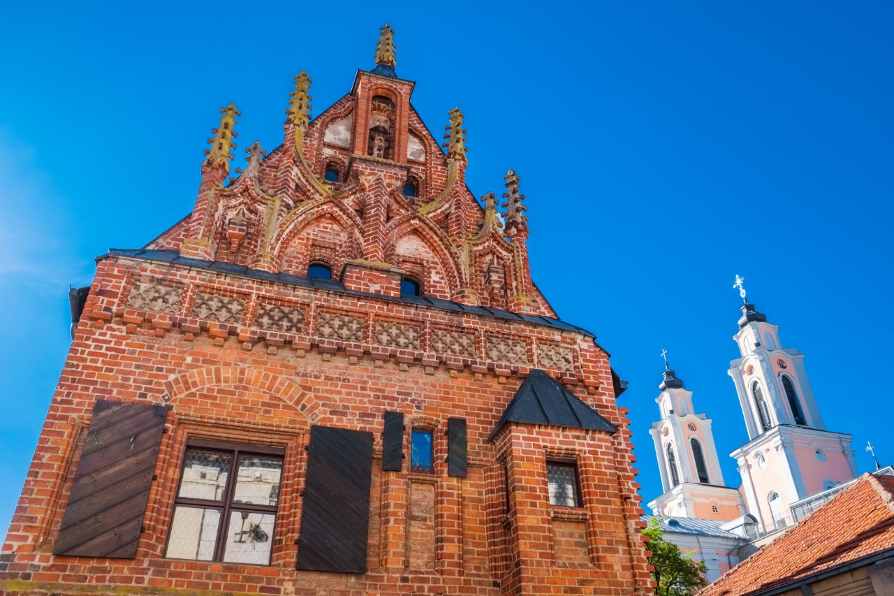 Front view of a historic building with red bricks and church towers in the background 