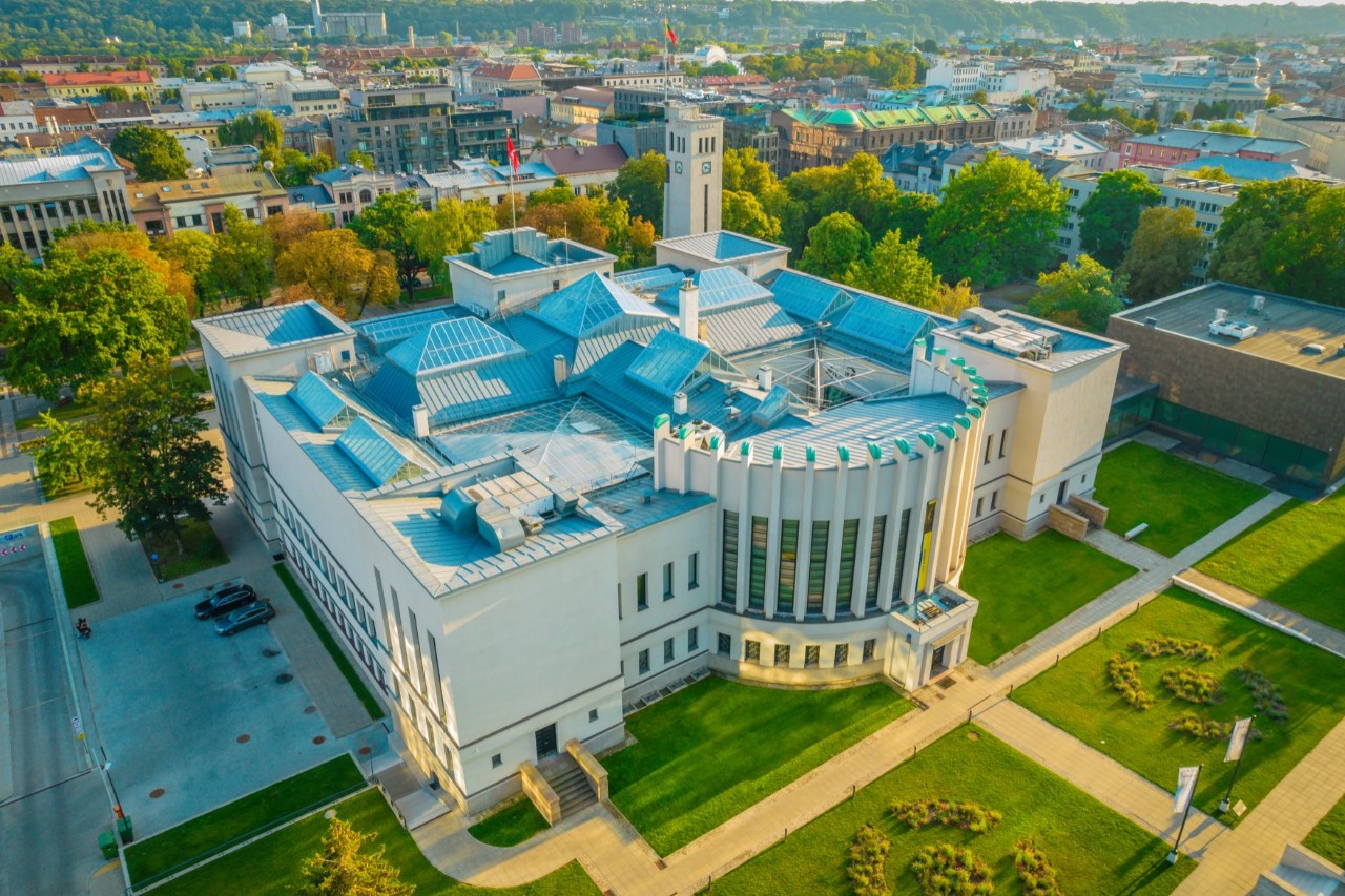 View from above of a white, massive museum building in a green area with houses in the background 
