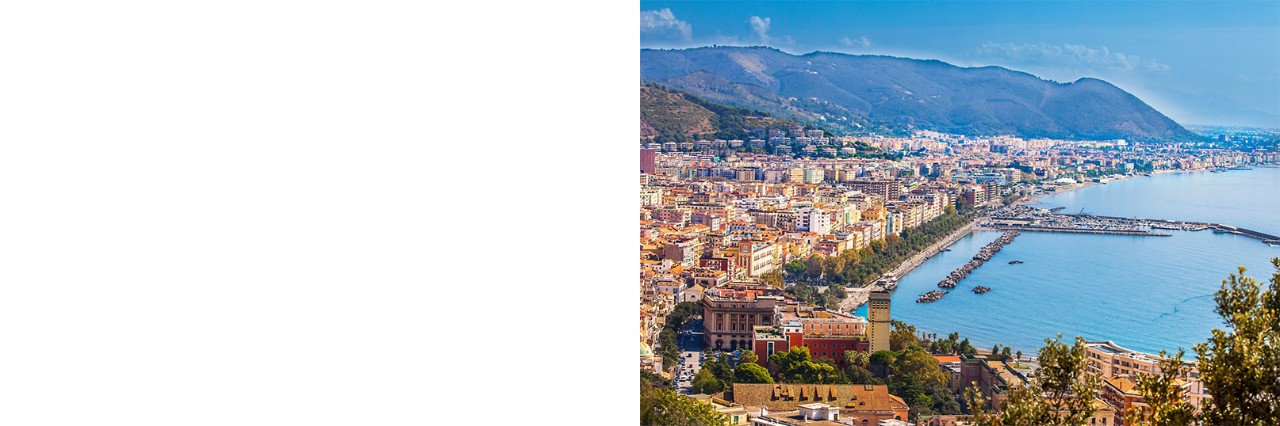 Salerno by the sea with a spacious harbour built into the sea. A mountain range can be seen in the background.