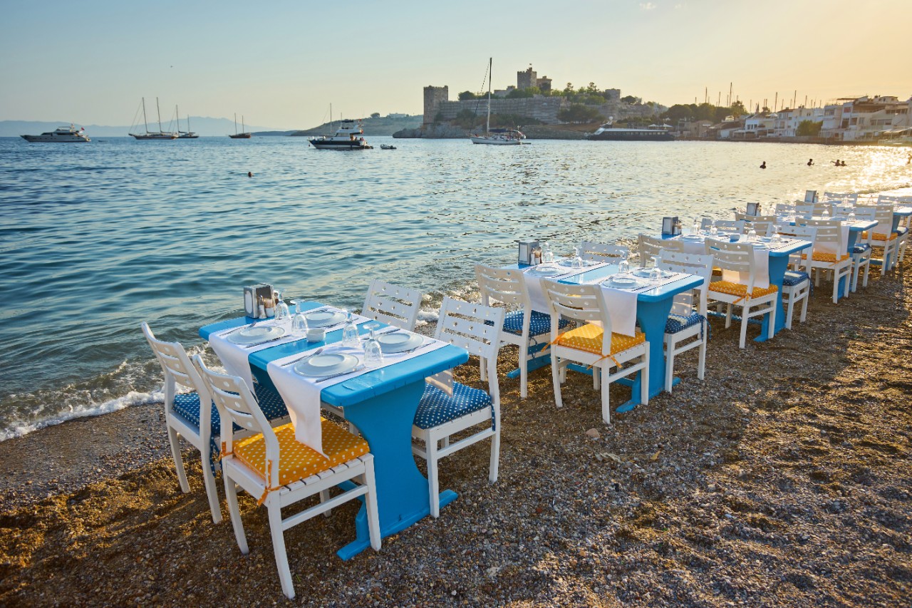 Restaurant-Tische, die direkt am Strand aufgestellt sind, mit Blick auf die Bucht.