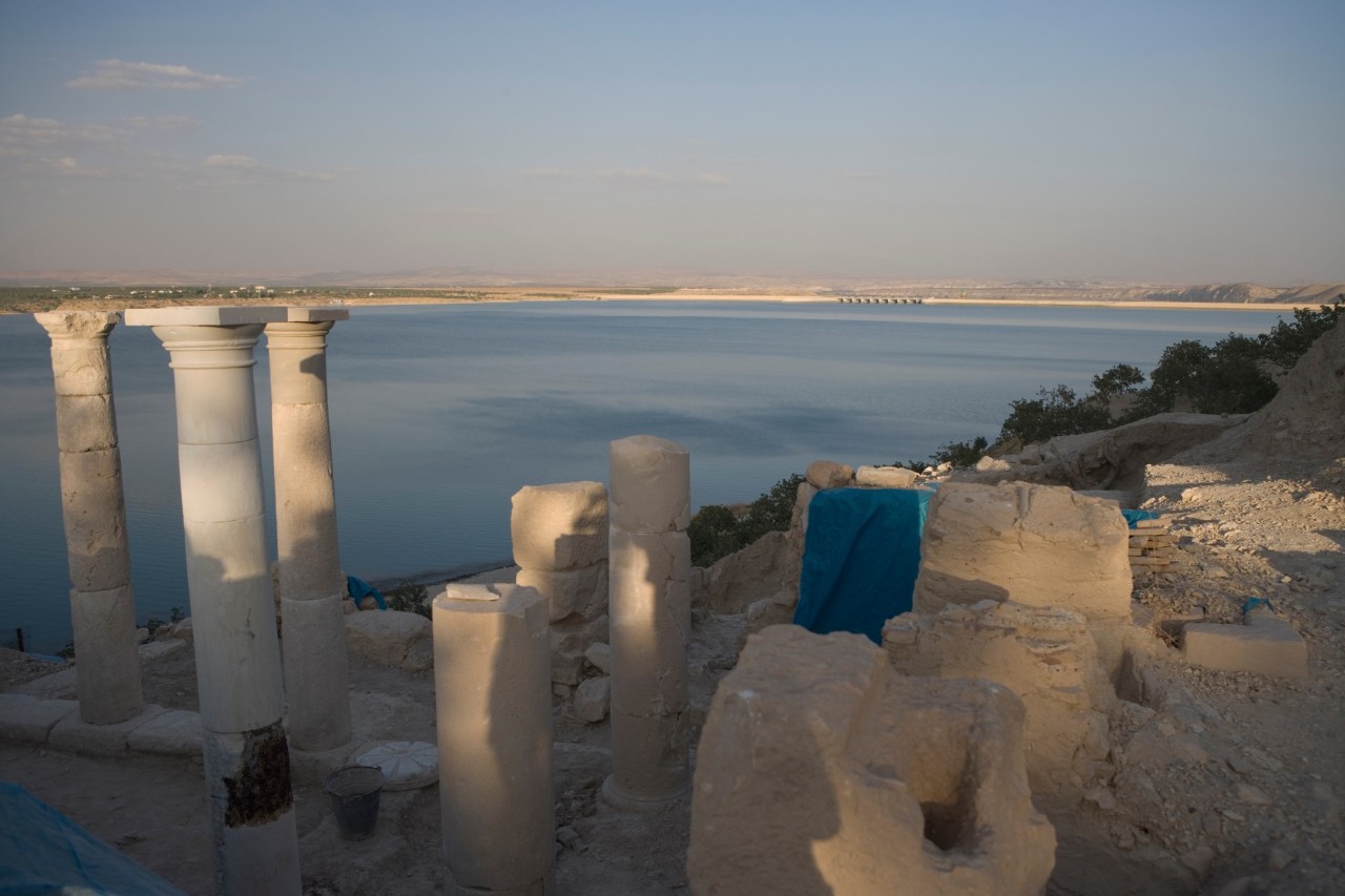 Several old stones and ancient columns on the bank of a wide river.