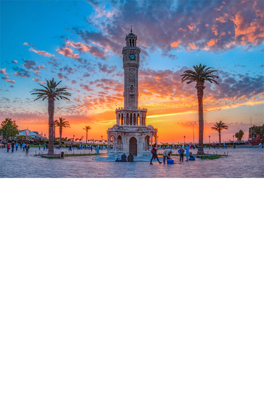 View of a tall, slender, richly decorated clock tower made of light-coloured stone.