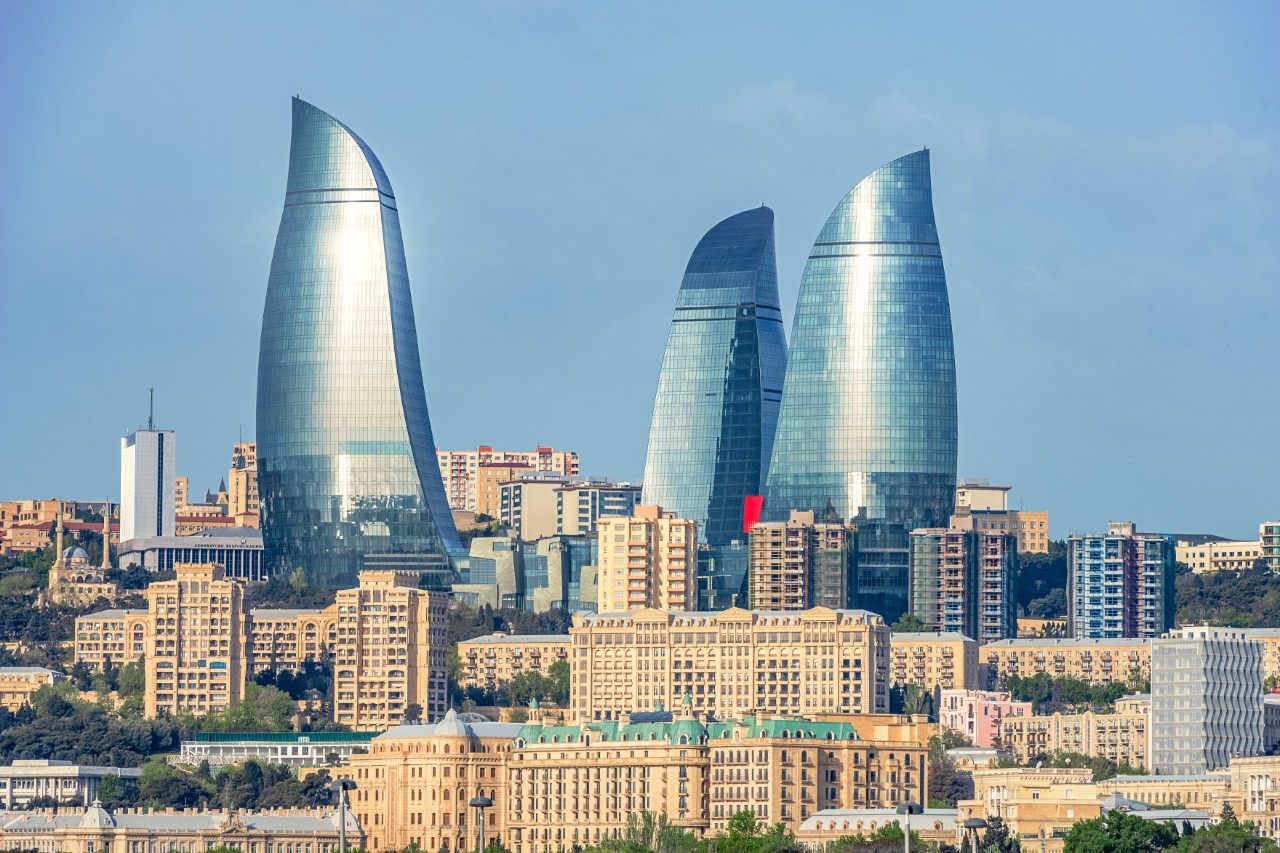 Three mirror-glass, flame-shaped high-rises rise up into the sky amidst other multi-storey, sand-coloured apartment blocks.