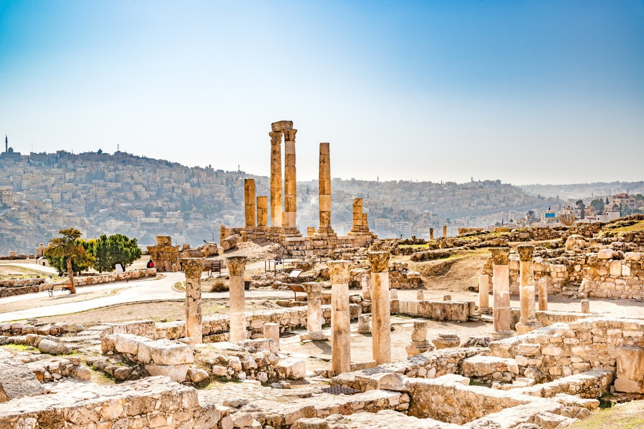 The picture shows an archaeological excavation site with the ruins and temple columns taking centre stage. The densely built-up city stretches out in the background on two hills.