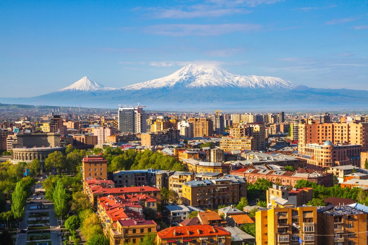 View over the roofs, streets, residential and high-rise buildings and green spaces of a city to a snow-covered mountain panorama.