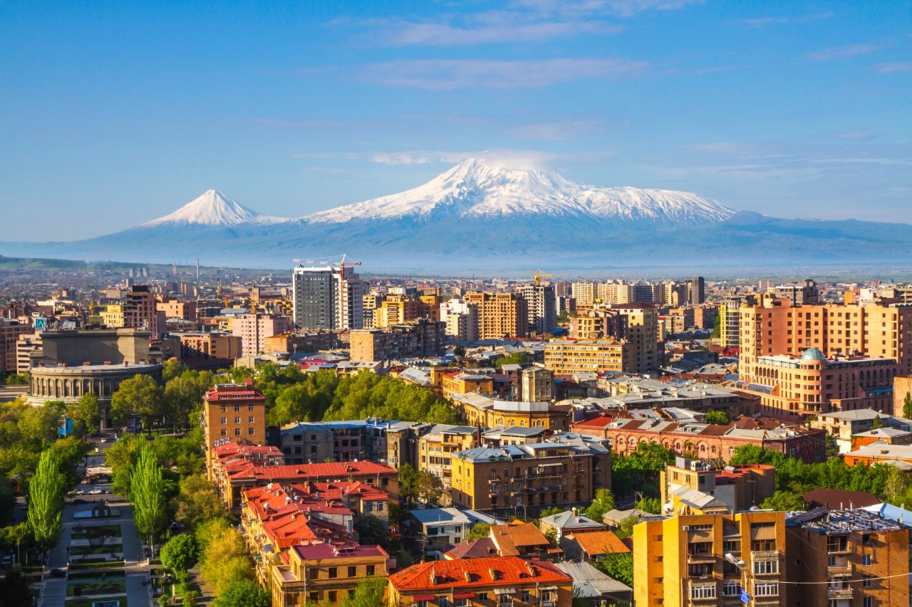 The roofs, streets, residential and high-rise buildings and green spaces of a city to a snow-covered mountain panorama.