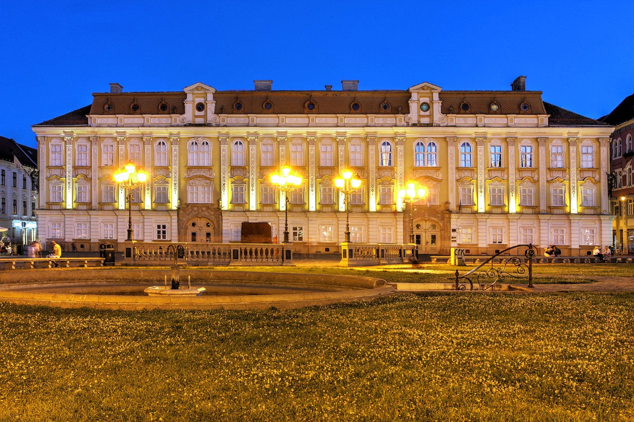 Illuminated two-storey palace in the evening with deserted park in the foreground.