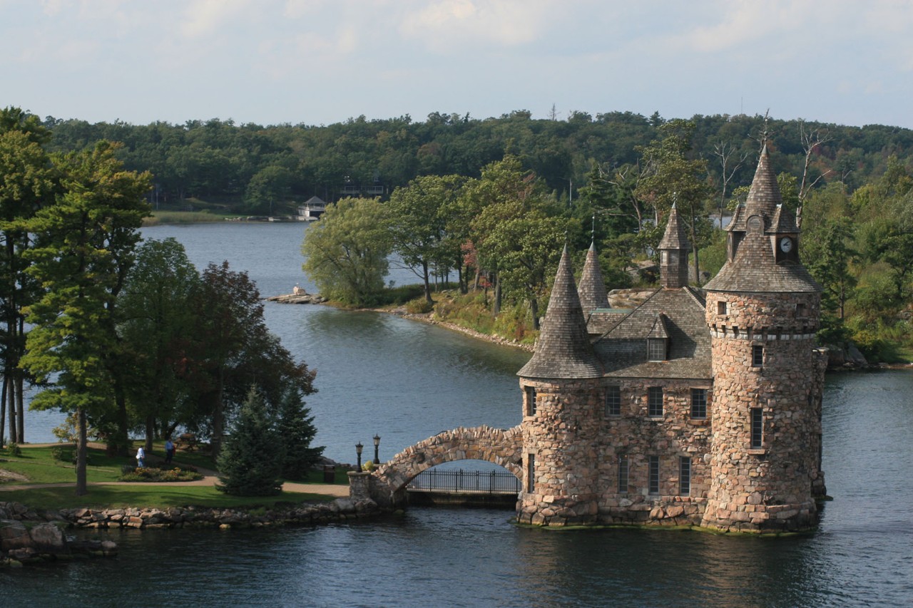 Moated castle with bridge to the shore in the middle of a river and trees.