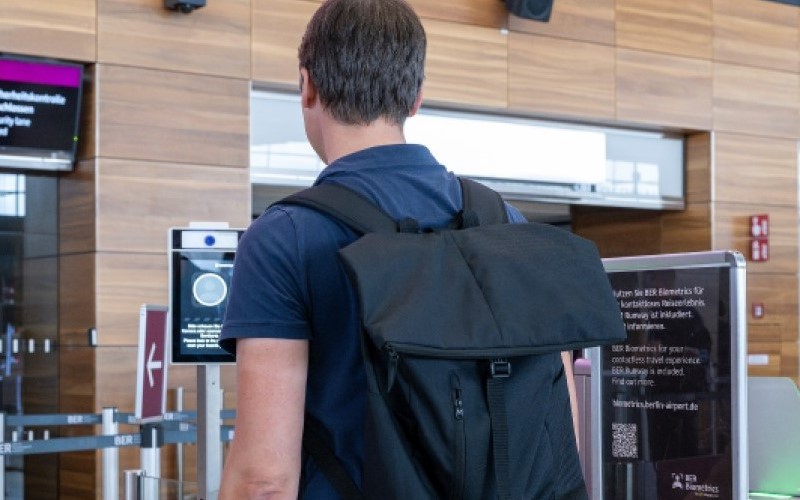 Person with rucksack from behind. Looks into a camera.