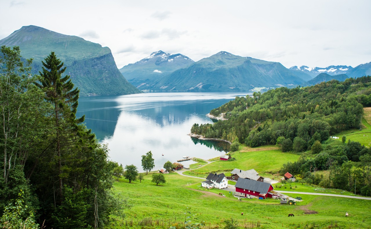 Red farm by a fjord in Norway seen from a distance.