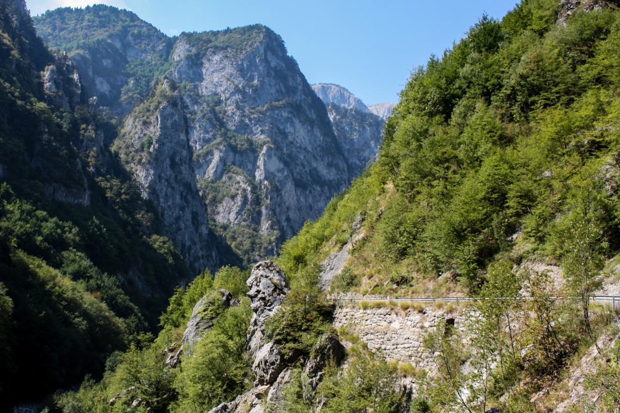 The picture shows a mountain landscape with a gorge running through it. On the mountain on the right-hand side of the picture, there is a path secured by a wall on the steep slope.