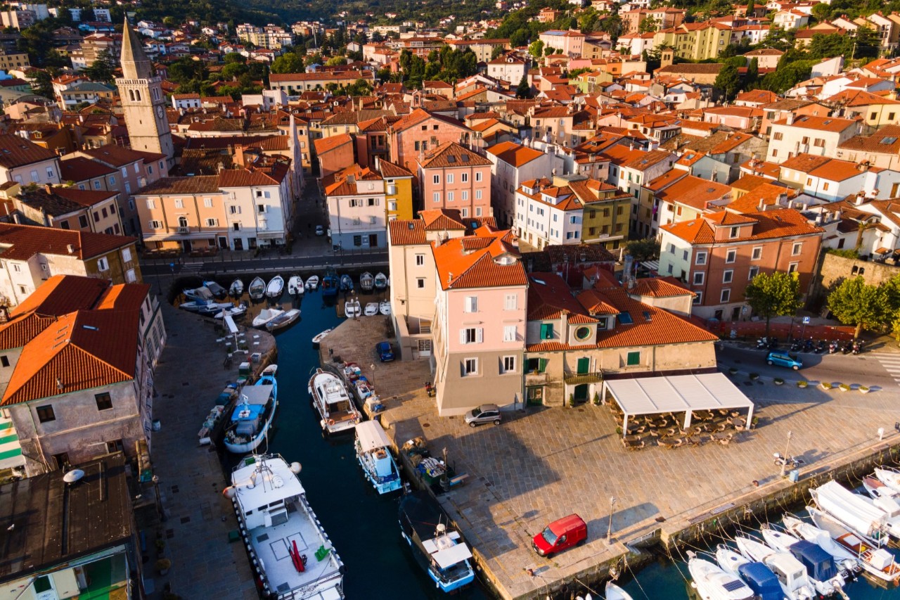 A densely built-up town with red rooftops, a church and small boats in the harbour.