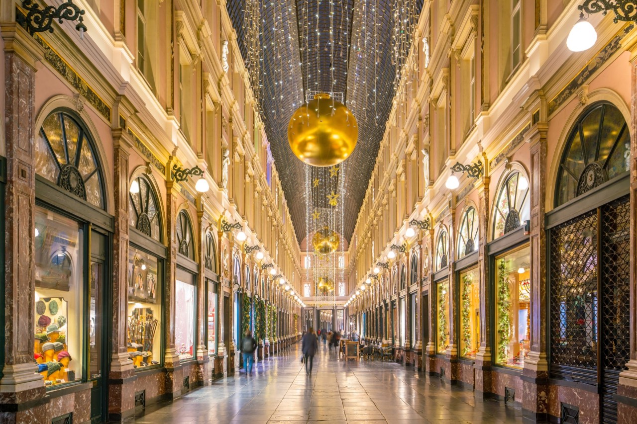 Interior view of the Galeries Royales Saint-Hubert shopping arcade, shops on the left and right, decorated for Christmas, golden lights, glass roof 