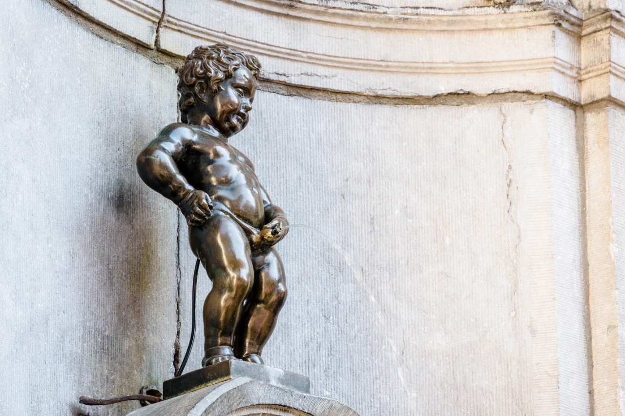 Bronze statue of Manneken Pis in front of a white marble wall 