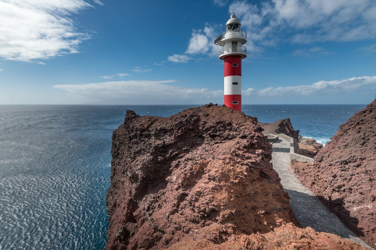 Red-and-white lighthouse surrounded by lava rock on the coast of Tenerife 