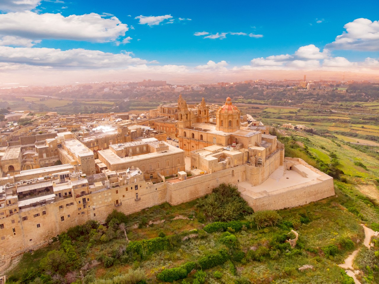 Aerial view of Mdina on a plateau with churches and palaces inland.