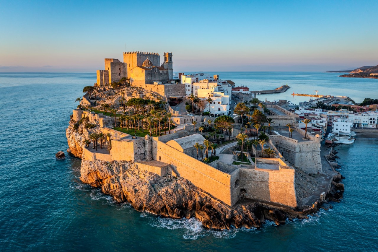 Island rising in the sea at dusk with a castle and city wall built upon it 