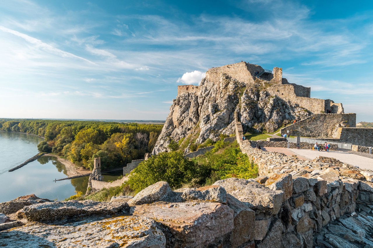 The castle ruins are on the right in the foreground, surrounded by green forests and rivers.