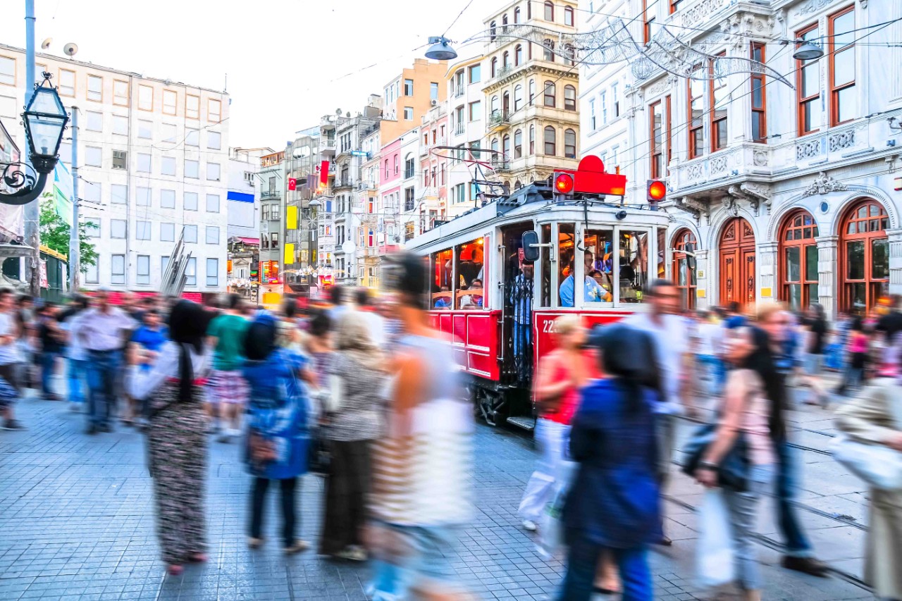 Crowd in İstiklal Caddesi shopping street with shops and lights.