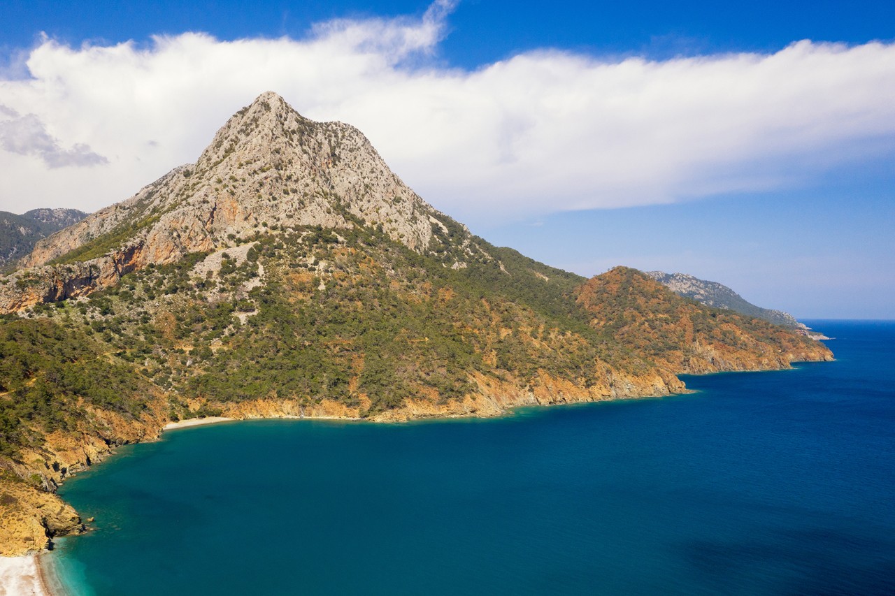 Rocky, partly wooded coastal landscape with a striking mountain rising directly from the deep blue sea.