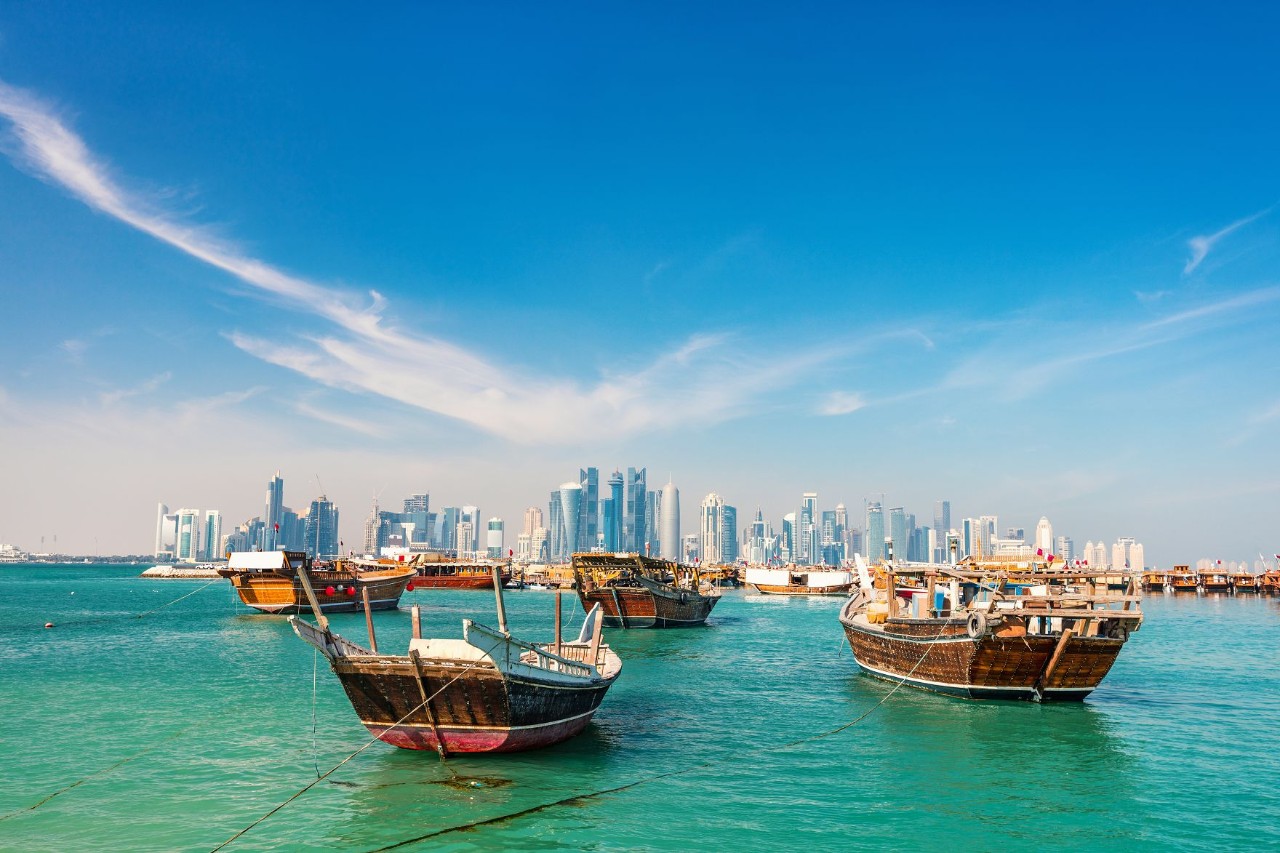 Boats on the water in front of Qatar’s skyline under clear skies.