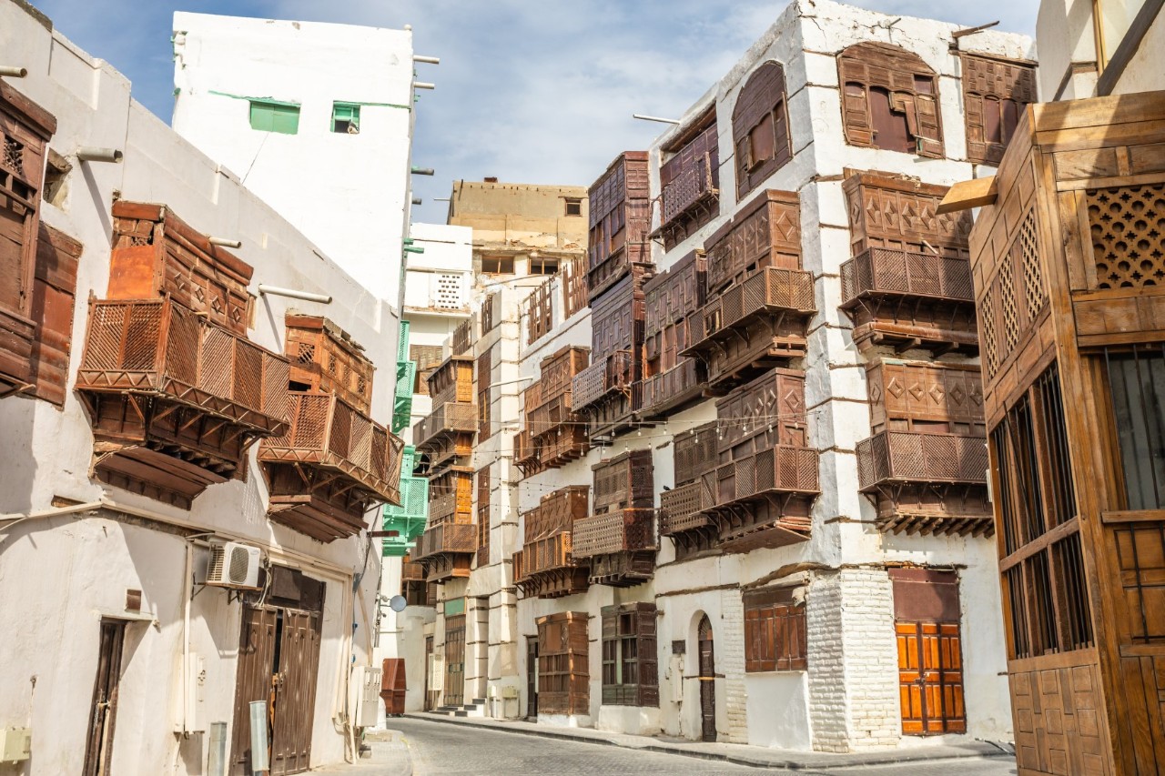 A winding street with white buildings with wooden balconies and blinds on the façades. 