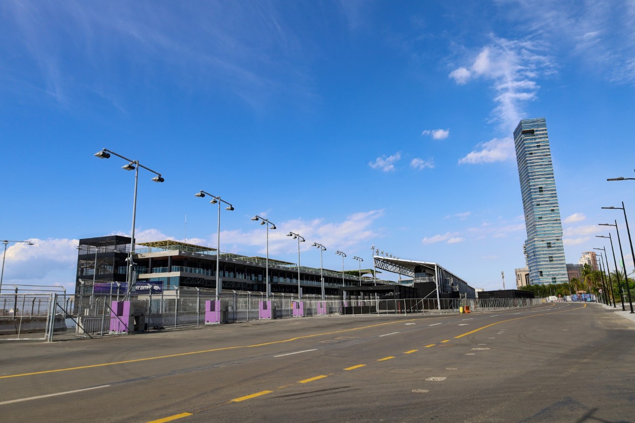 The outside of the entrance to the race track area with buildings, tower and street lamps.  