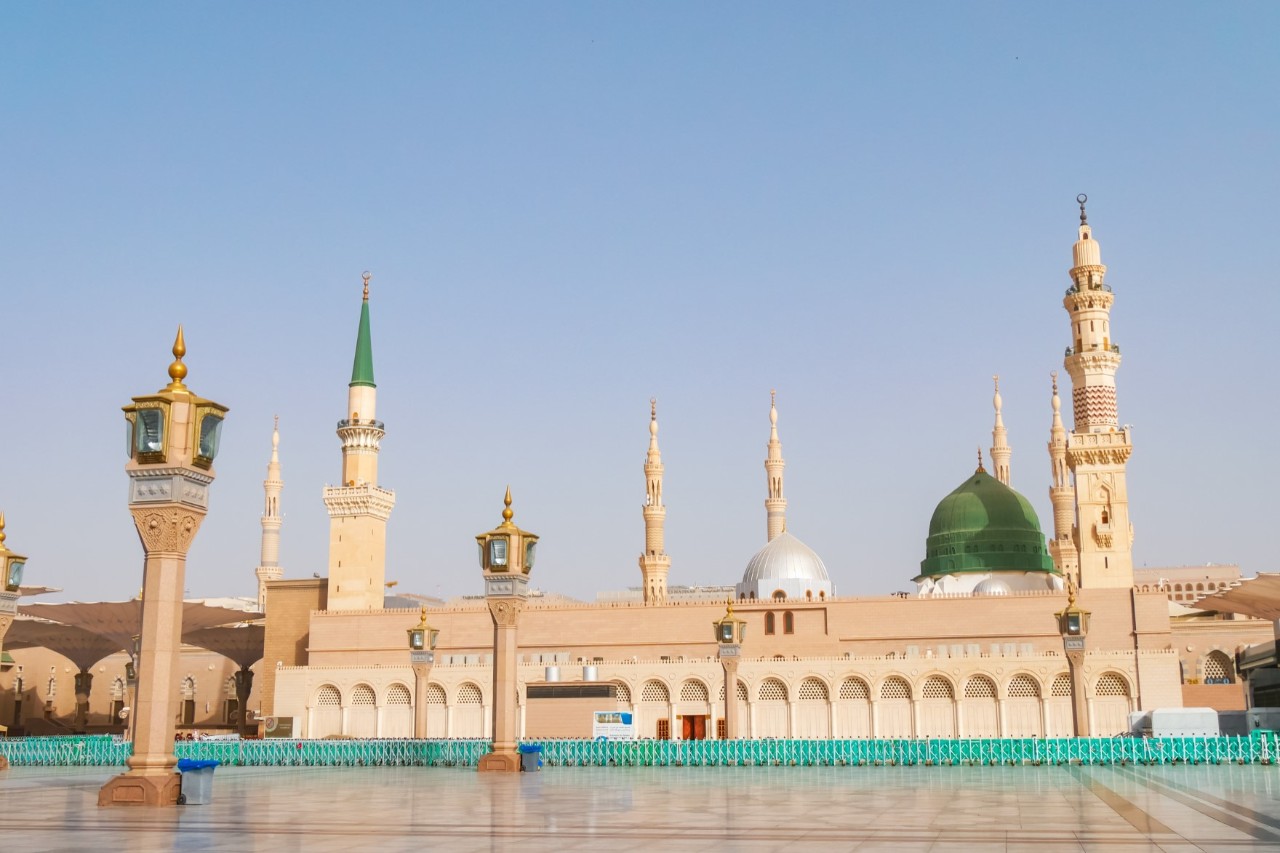 The deserted forecourt of the beige Prophet’s Mosque with minarets and street lamps. 