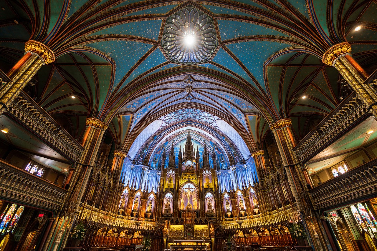 Interior view of Notre-Dame Basilica in Montréal with blue starry sky, neo-Gothic altar and ornate details bathed in warm light.