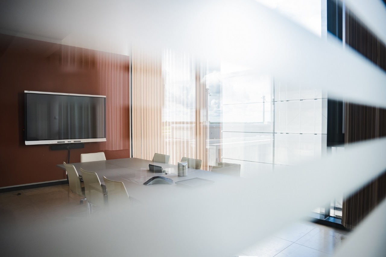 View through a glass pane into a conference room with TV, table and chairs around it.