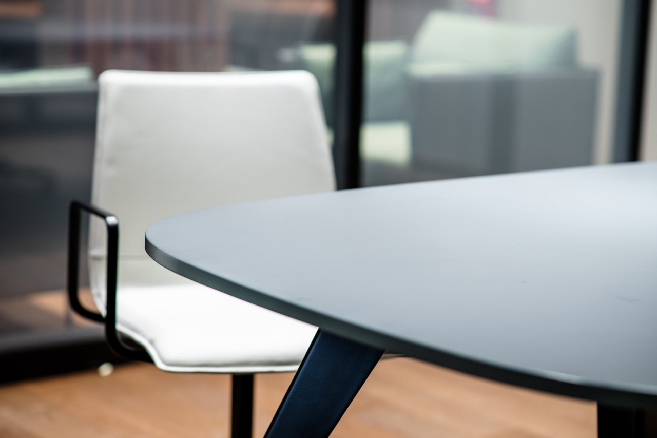 View of a chair in front of a table in a separate conference room with a transparent window to the lounge.