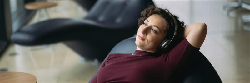A woman in her mid-30s is lying in a BER lounge chair listening to music through headphones.