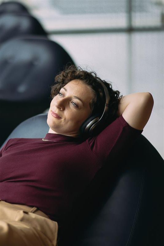 A woman in her mid-30s is lying in a BER lounge chair listening to music through headphones.