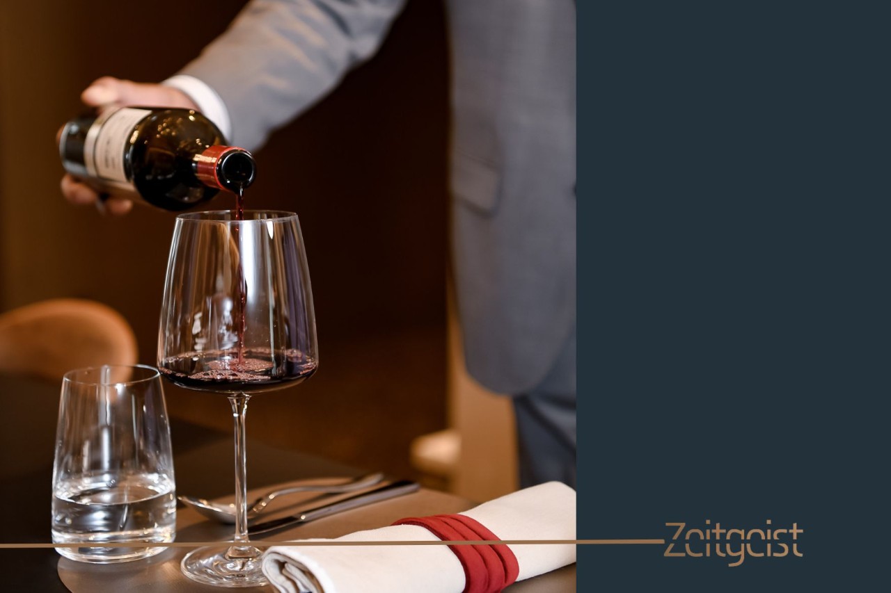 VIP service employee pours red wine into a wine glass. Next to it is a glass of water.
