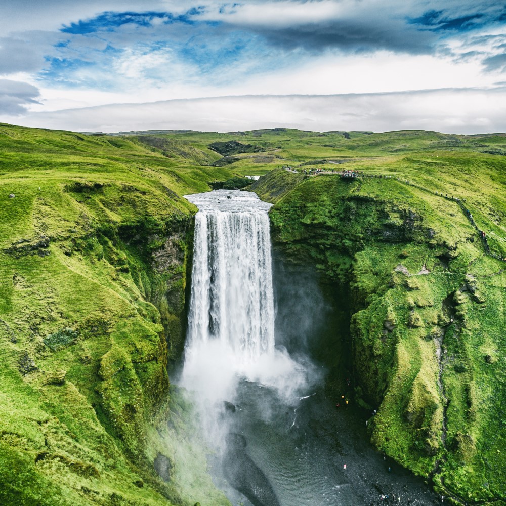 Green meadow landscape. A waterfall in the centre. Cloudy sky.