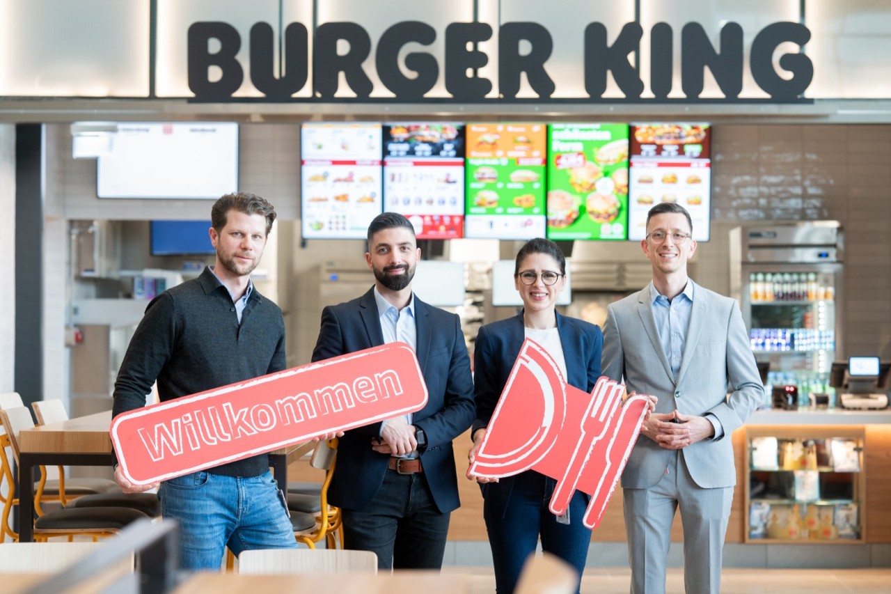 4 people holding signs in front of a Burger King branch