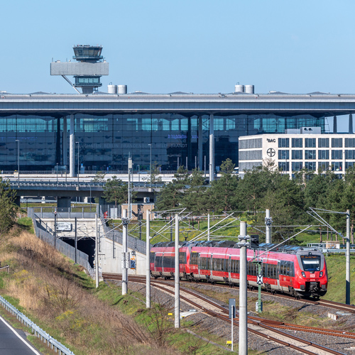 Bahn fährt aus dem Flughafenbahnhof aus. Im Hintergrund das Terminal 1 und der Tower.