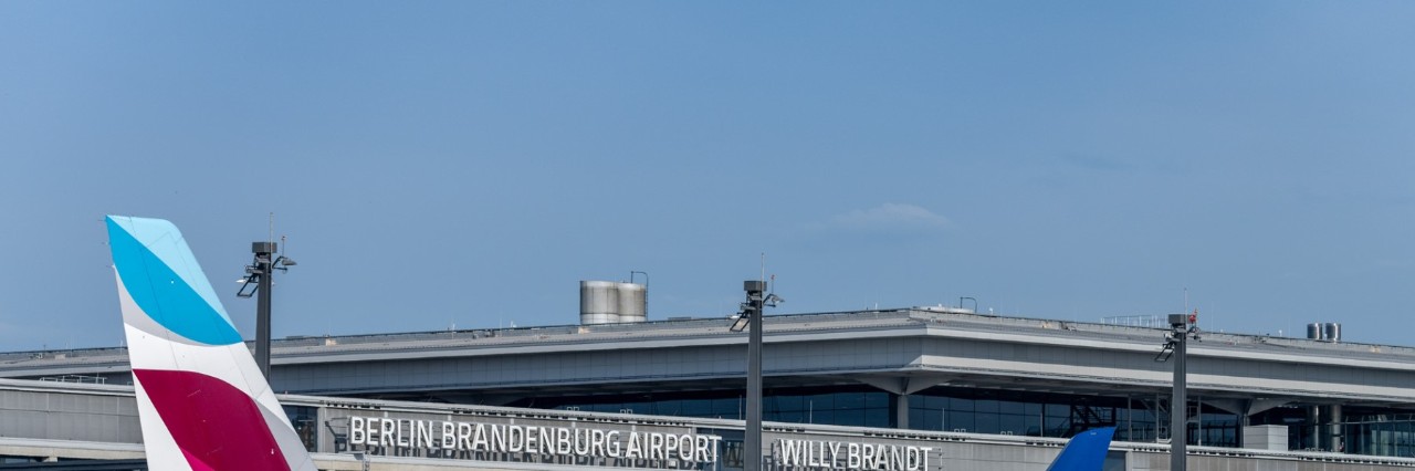 Tail of a Eurowings aircraft in front of the lettering ‘Berlin Brandenburg Airport Willy Brandt’ on the airside front of BER Terminal 1