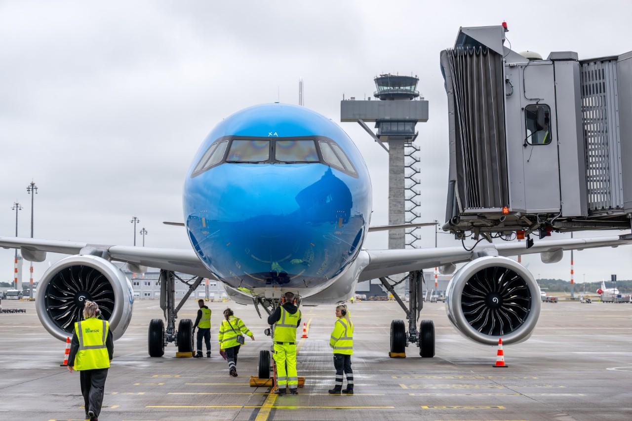 Nose of a KLM aircraft. In the foreground, employees with high-visibility waistcoats.