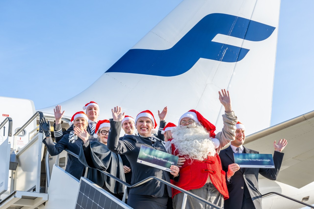 Santa Claus and an aeroplane crew stand on an aeroplane staircase and wave.