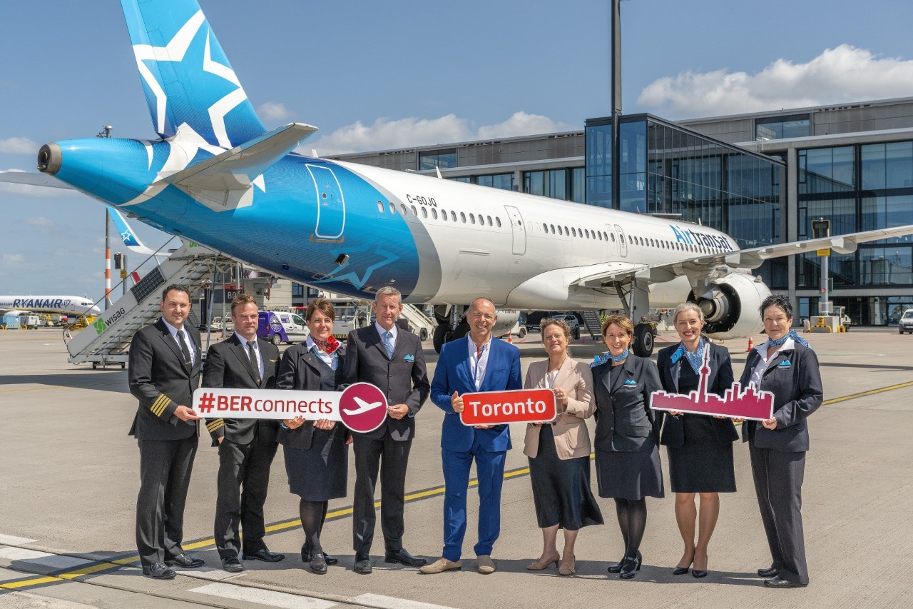 A group of people are standing in front of an aircraft holding signs in their hands.