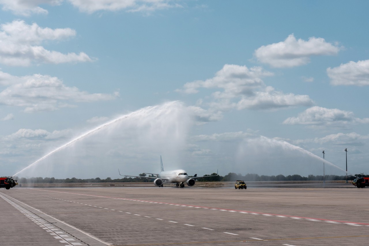 A plane belonging to the airline Air Transat is taxiing on the apron, with water fountains arching over the aircraft.