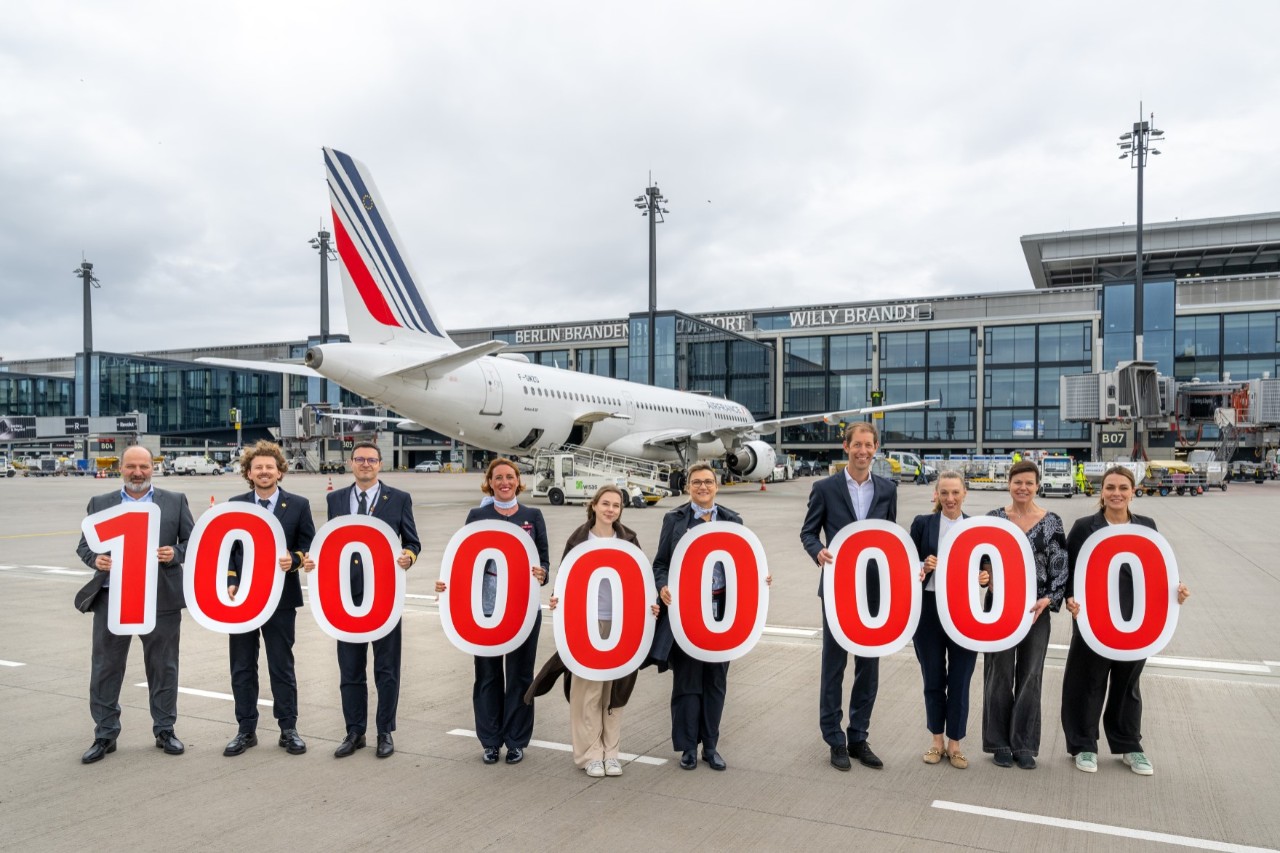 A group of people pose with signs on the apron in front of an aircraft.